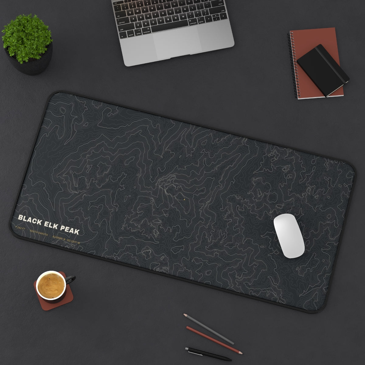Black Elk Peak Topo desk mat on a desk with a laptop, mouse and coffee cup for scale