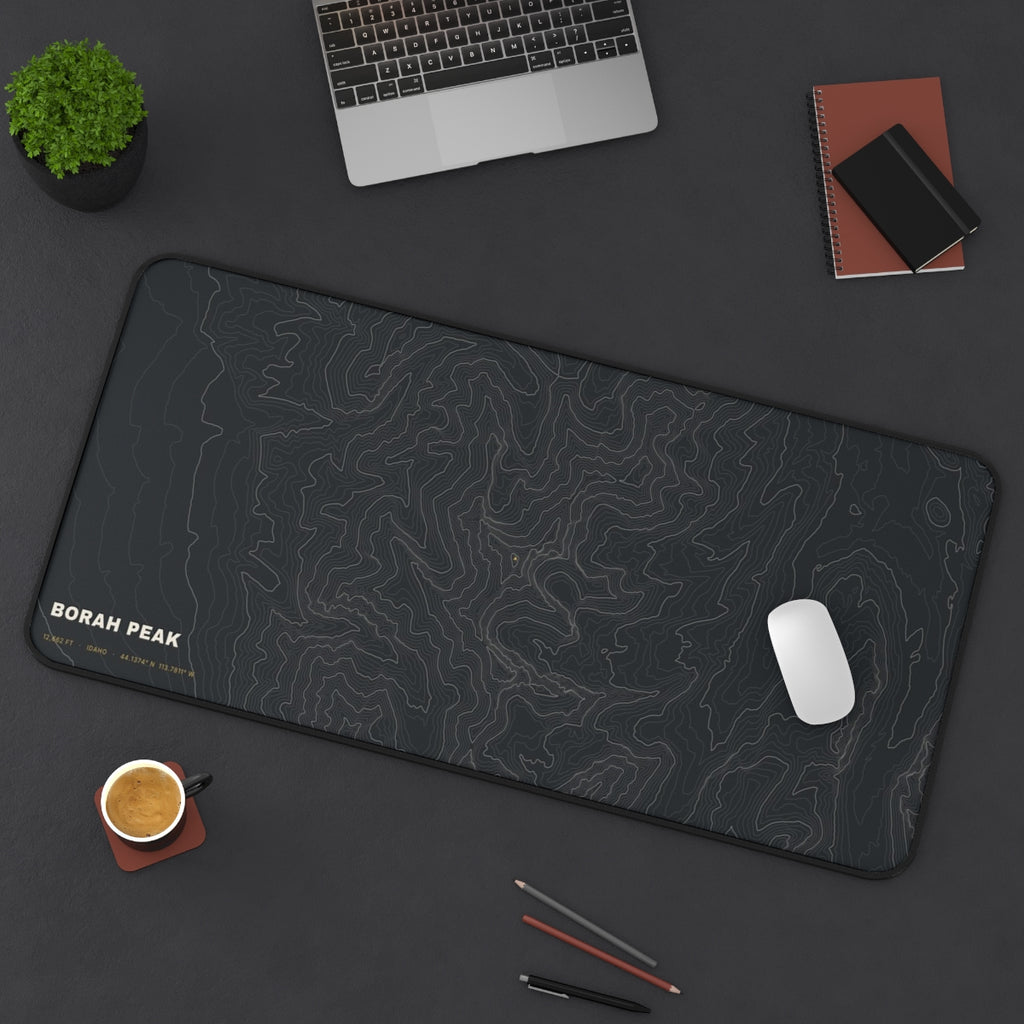 Borah Peak Topo desk mat on a desk with a laptop, mouse and coffee cup for scale