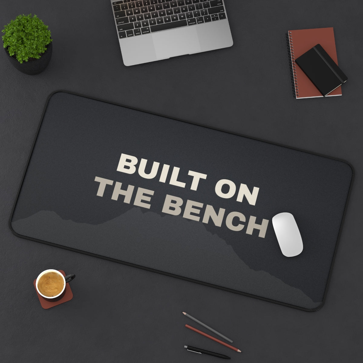 Built on the Bench desk mat on a desk with a laptop, mouse and coffee cup for scale