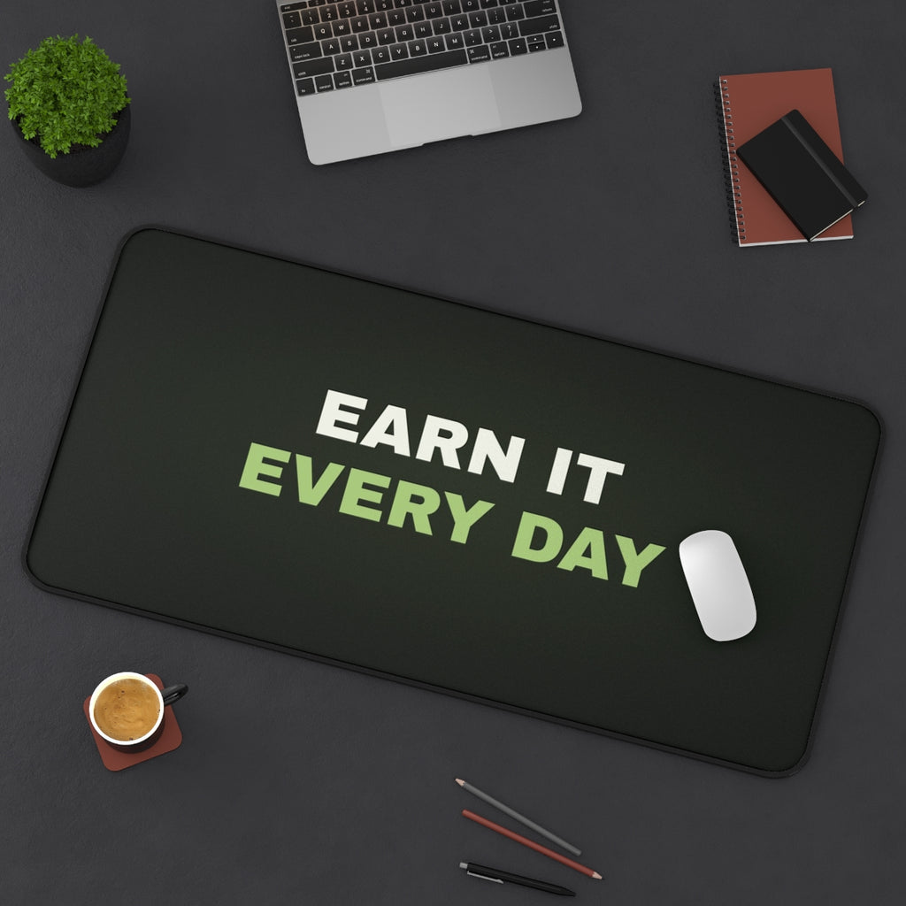 Earn It Every Day desk mat on a desk with a laptop, mouse and coffee cup for scale