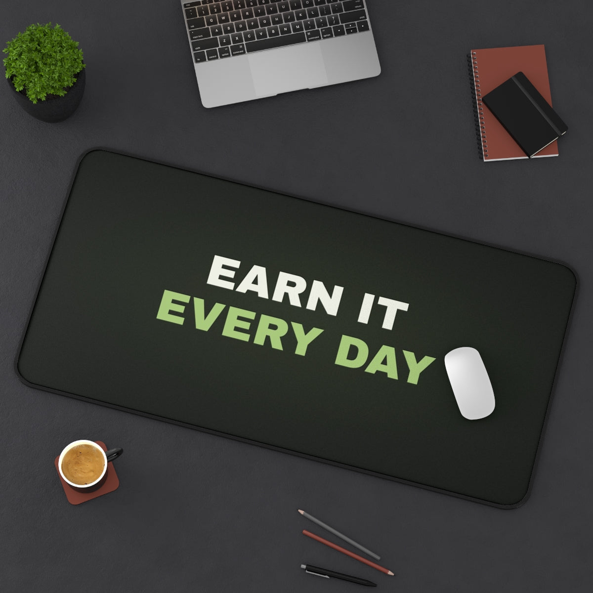 Earn It Every Day desk mat on a desk with a laptop, mouse and coffee cup for scale