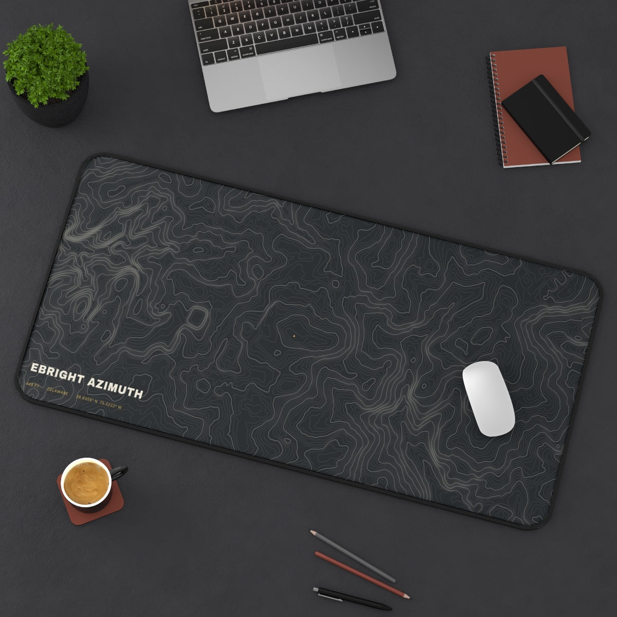 Ebright Azimuth Topo desk mat on a desk with a laptop, mouse and coffee cup for scale