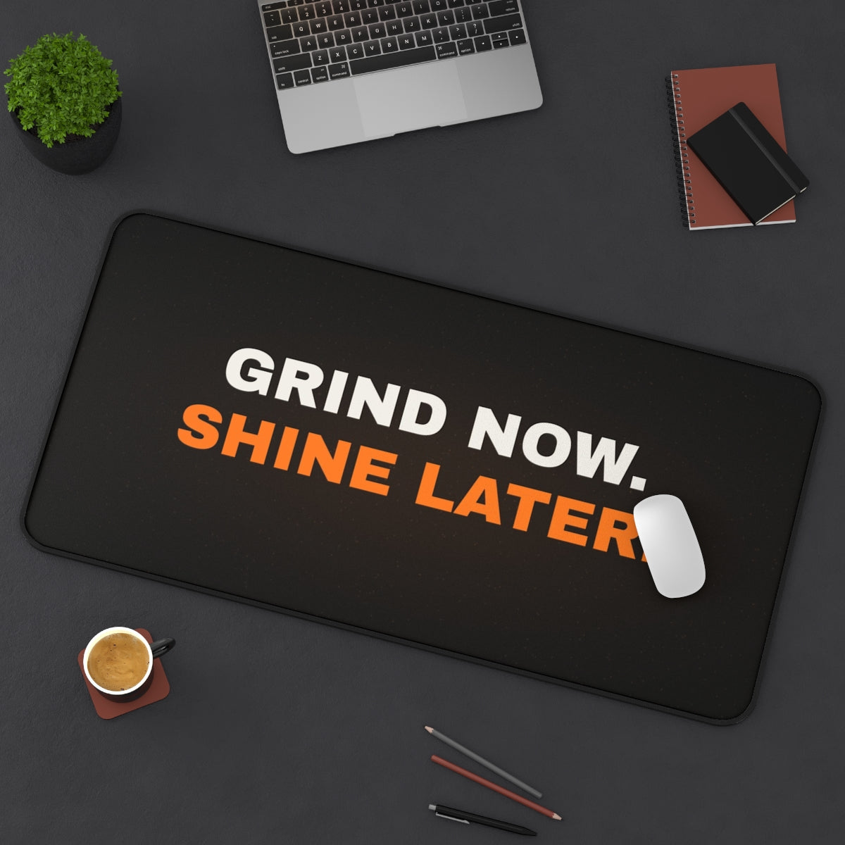 Grind Now Shine Later desk mat on a desk with a laptop, mouse and coffee cup for scale