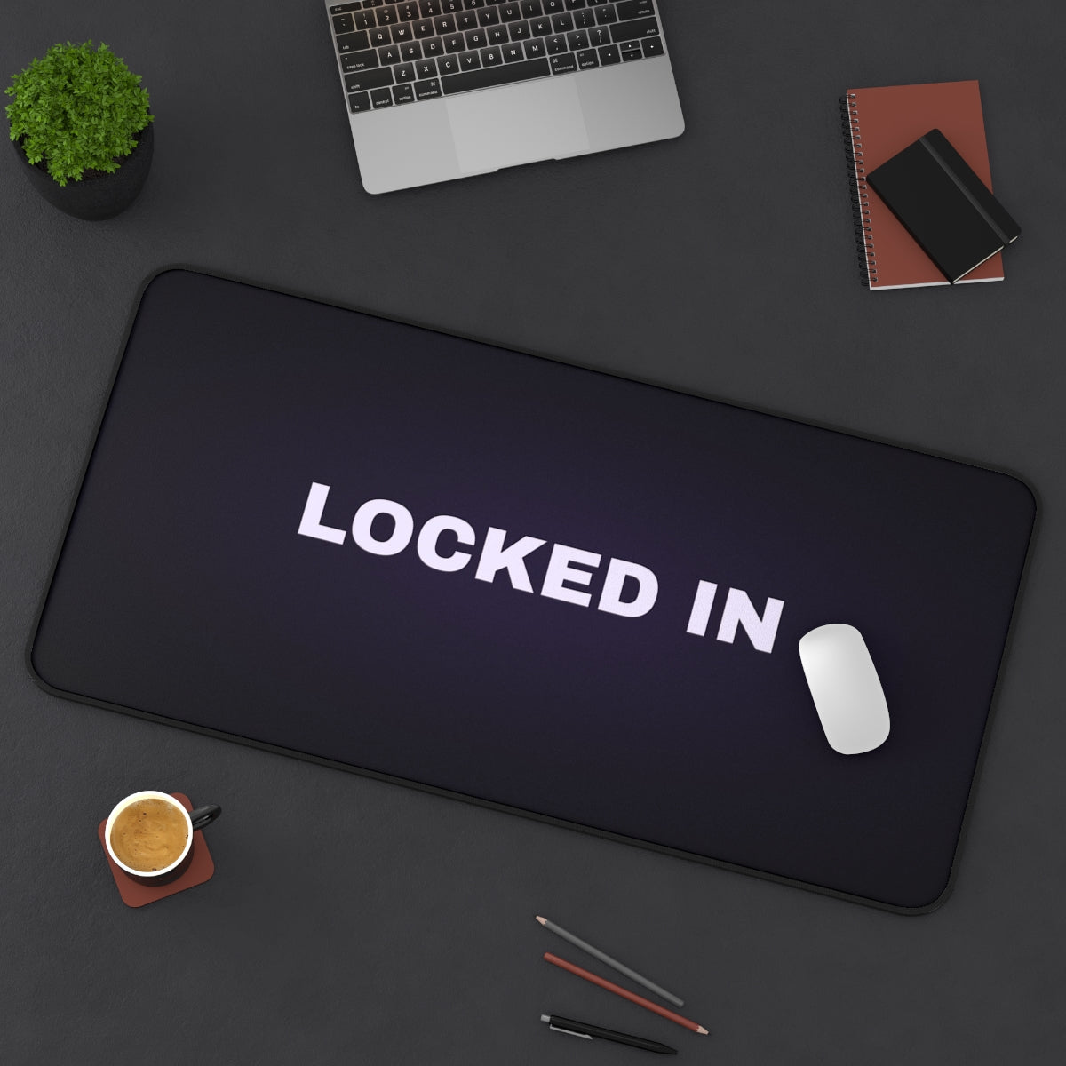 Locked In desk mat on a desk with a laptop, mouse and coffee cup for scale
