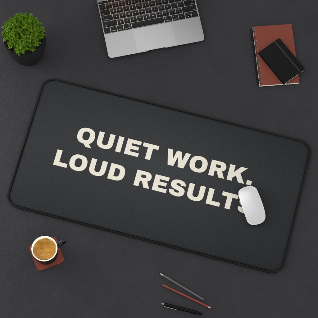 Quiet Work Loud Results desk mat on a desk with a laptop, mouse and coffee cup for scale