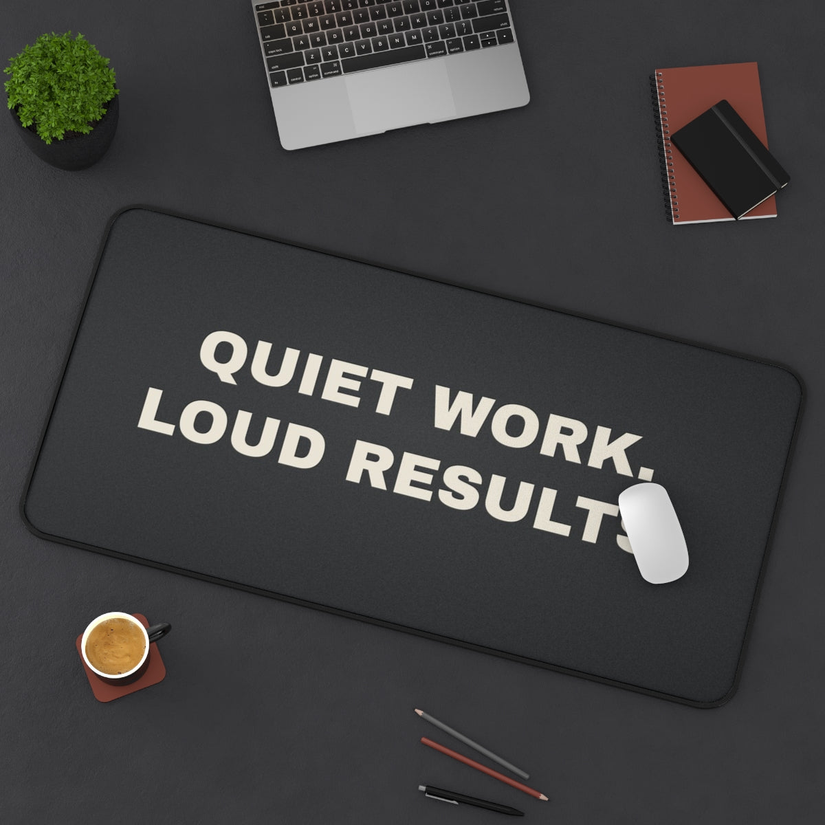 Quiet Work Loud Results desk mat on a desk with a laptop, mouse and coffee cup for scale